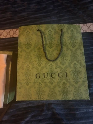 Beige Gucci bälte med monogram - Säljer ett beige bälte från Gucci med det klassiska GG-monogrammönstret längs hela bältet. Bältet har silverfärgat spänne och kommer med originalpåse och grön presentpåse från Gucci. Perfekt accessoar för att lyfta din outfit.