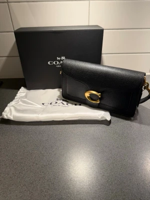 Coach Tabby - Snygg svart handväska från Coach i strukturerat läder med avtagbar axelrem och guldfärgat C-spänne framtill. Väskan har stilren design och levereras med dustbag och originalask. Perfekt för dig som gillar klassiska accessoarer med lyxig känsla.