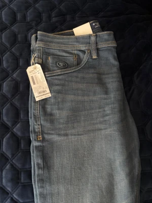 Blå raka jeans med etikett - Säljer ett par klassiska blå jeans med raka ben och normal midja. Jeansen har fem fickor, kontrastsömmar och är tillverkade i ett mjukt denimtyg. Perfekta för en avslappnad och stilren look. Etiketten sitter kvar.
