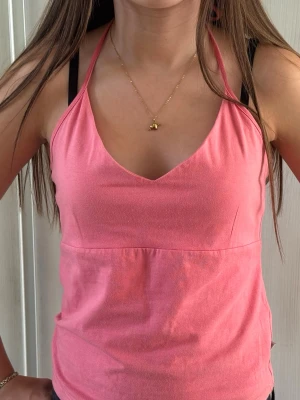 Rosa halterneck linnetopp - Säljer en rosa halterneck linnetopp med v-ringning och smala axelband. Toppen har en enkel och stilren design, perfekt för varma dagar. Materialet känns mjukt och lätt mot huden.