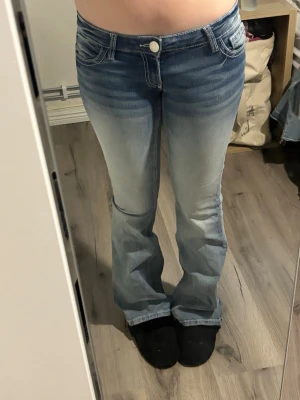 Blå bootcut jeans med broderade fickor - Säljer ett par ljusblå bootcut jeans med broderade detaljer på bakfickorna. Jeansen har låg midja och klassisk femficksmodell. Perfekta för dig som gillar en avslappnad men trendig stil. Lite slitna vid gylfen men ingenting som syns och som kan lagas innan leverans. Säljer då de tyvärr är för stora