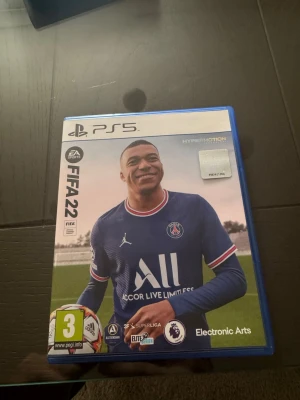 FIFA 22 till PS5 - FIFA 22 till PlayStation 5 med blå plastfodral. Omslaget visar Kylian Mbappé i PSG-tröja. Spelet har HyperMotion-teknik och är PEGI 3-märkt. Perfekt för dig som gillar fotbollsspel och vill spela med lag från olika ligor.