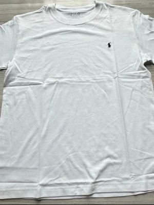 Vit t-shirt från Polo Ralph Lauren - Klassisk vit t-shirt från Polo Ralph Lauren med rund hals och korta ärmar. T-shirten har den ikoniska broderade loggan på bröstet och är tillverkad i mjuk bomull för en skön känsla. Perfekt basplagg till alla outfits.