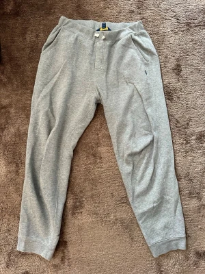Gråa mjukisbyxor från Polo Ralph Lauren - Snygga gråa mjukisbyxor från Polo Ralph Lauren med klassisk broderad logga på benet. Byxorna har dragsko i midjan, muddar vid bensluten och två sidofickor. Tillverkade i mjukt sweatshirtmaterial som är riktigt skönt.
