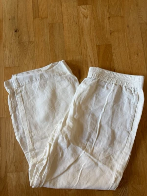 Vita linnebyxor med resårmidja - Säljer ett par vita linnebyxor med avslappnad passform och resår i midjan. Byxorna har raka ben och sidofickor. Perfekta för en chill och stilren look under varma dagar.