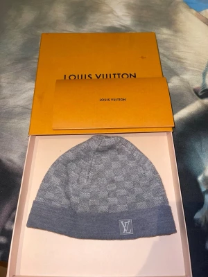 Louis Vuitton mössa  - Snygg grå mössa från Louis Vuitton med diskret rutmönster och LV-logga framtill. Tillverkad i mjuk ullmix som känns lyxig och bekväm. Perfekt accessoar för dig som vill ha en exklusiv touch på din outfit.