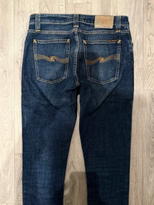Nudie Jeans Skinny Lin Mörkblå W29/L32 - Slim/Skinny Fit - Nudie Jeans Skinny Lin ”Flat Love” mörkblå jeans med slim/skinny passform, normalhög midja och smala, avsmalnande ben, storlek W29/L32, midja 37,5 cm, ytterbenslängd 105 cm, benöppning 14 cm, modellen är 185cm & väger 65kg, i fint skick.