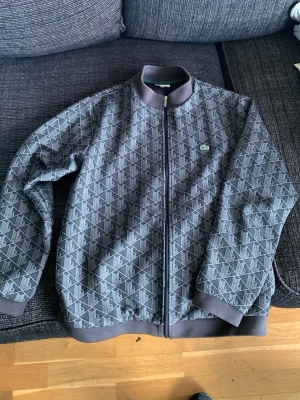 Grå mönstrad hoodie från Lacoste - Snygg grå hoodie från Lacoste. Passar en vuxen S