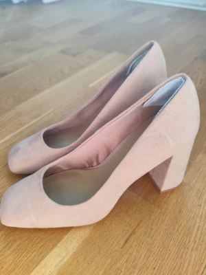 Ljusa rosa pumps med bred klack - Snygga pumps i ljusrosa mockaimitation med bred, stabil klack och rundad tå. Skorna har en stilren och modern look som passar till många olika outfits. Perfekta för dig som vill ha både höjd och komfort.