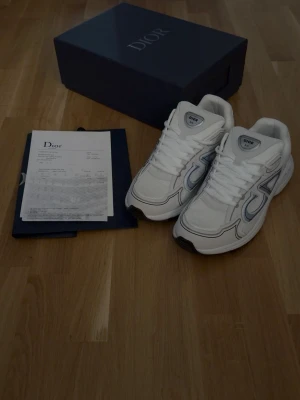 Vita Dior B30 - Säljer ett par vita Dior sneakers med grå detaljer. Perfekta för dig som vill ha en exklusiv och trendig look.