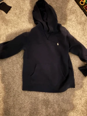 Mörkblå hoodie från Polo Ralph Lauren - Snygg mörkblå hoodie från Polo Ralph Lauren med klassisk huva och känguruficka. Liten broderad logga på bröstet. Tillverkad i mjukt material som känns skönt mot huden. Perfekt för en avslappnad och stilren look. Pris kan sänkas lite