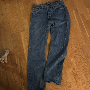 Levi's 501 blå jeans W30 L32 - Klassiska Levi's 501 jeans i blå denim med raka ben och fem fickor. Jeansen har knappgylf, bruna sömmar och den ikoniska läderpatchen bak i midjan. Perfekt för dig som gillar tidlös stil och vill ha ett par schyssta jeans med autentisk känsla.