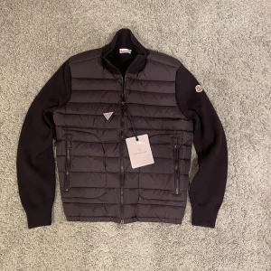 Svart Moncler cardigan - Säljer denna Moncler cardigan i svart färg den kommer med tags och nfc funkar. Den är i helt nytt skick och det finns inga konstigheter med den alls. Den är i storlek M.