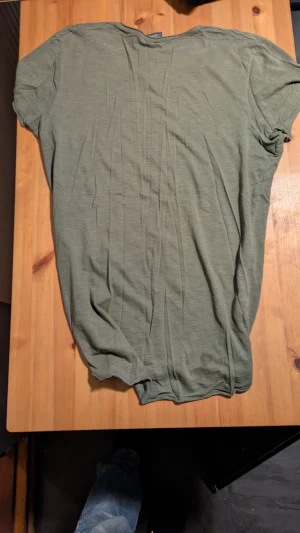 Olivgrön old school t-shirt från Jack & Jones - Snygg olivgrön t-shirt från Jack & Jones Originals med klassisk rund hals och korta ärmar och lång. T-shirten är tillverkad i mjuk bomull och har en enkel, stilren design utan mönster eller detaljer. Perfekt för dig som gillar en clean och avslappnad look, breda axlar och vill se slim/vältränad ut. 