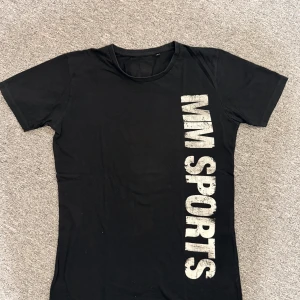 Svart MM Sports t-shirt i bomull - Svart t-shirt från MM Sports med stort vitt tryck både fram och bak. Materialet är 100% bomull. Hör av dig vid frågor eller behov av fler bilder!