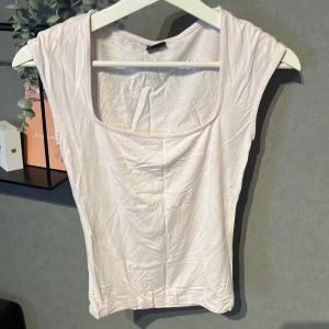 Ljusrosa ärmlös topp med fyrkantig hals - Säljer en ljusrosa topp med snygg fyrkantig halsringning och ärmlös design. Toppen är figurnära och gjord i mjukt bomullsmaterial, perfekt för en clean och enkel look. Passar dig som gillar minimalistisk stil och ljusa färger.