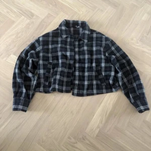 Svartvit rutig croppad skjorta - Croppad skjorta i svart och vitt med rutigt mönster. Skjortan har långa ärmar, klassisk krage och knäppning framtill. Materialet är mjukt och känns som bomull, perfekt för en avslappnad och trendig look.