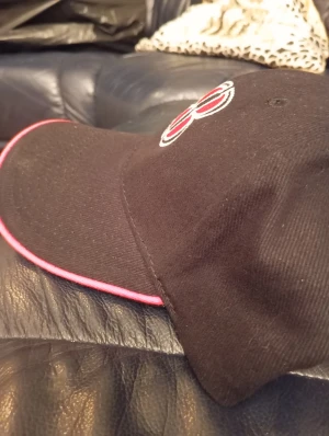 Svart keps med röd 88-brodyr - Svart keps med broderad 88 i rött och vitt framtill. Skärmen har en snygg röd kant som ger extra attityd. Klassisk form med böjd skärm, perfekt för dig som gillar sportig och cool stil. Materialet känns som bomull och kepsen har en stilren look.