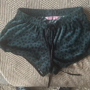 Mörkgröna leopardmönstrade shorts XS - Snygga mörkgröna shorts från Hunkemöller i storlek XS med leopardmönster och mjukt, glansigt material. De har elastisk midja och snörning framtill för skön passform. Perfekta för chill eller mysiga dagar hemma.