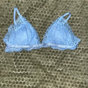 Ljusblå spetsig linnetopp - Säljer en ljusblå bh i spets med tunna axelband och vacker spetskant runt hela toppen. Bh:n har en triangelformad design och är helt ärmlös, perfekt för att skapa en söt och feminin look. Justerbara axelband för bästa passform. Har endast provat en gång men passade aldrig riktigt när jag köpte den, lappen är dock klippt 