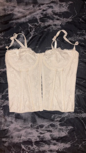 Vit spetskorsett från SHEIN, stl S - Säljer en vit korsett från SHEIN i storlek S. Toppen har vackra spetsdetaljer, justerbara axelband och snörning i ryggen för en snygg passform. Materialet är polyester och toppen har en croppad siluett med lätt v-ringad hals. Perfekt för dig som gillar romantisk och trendig stil.