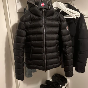 Svart Colmar pufferjacka med huva - Säljer en svart pufferjacka från Colmar med huva och dragkedja framtill. Jackan är vadderad och ser helt ny ut. Endast använd i 3 månader. Säljer pga att jag ej använder. Galje medföljer. Äkta såklart❤️(kommer inte vilja gå ned i pris)😁 storlek 42 IT (som en S)