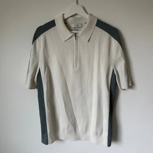 Vit pikétröja med dragkedja från COS - Snygg vit pikétröja från COS i relaxed fit med gråa paneler längs axlar och sidor. Tröjan har korta ärmar, klassisk krage och en stilren dragkedja framtill. Materialet är bomull med detaljer i viskos, polyamid och elastan för extra komfort. 5J4