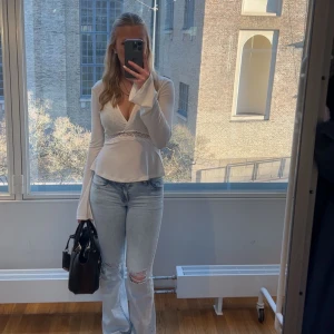 Vit topp med spets från Gina Tricot - Supersnygg vit topp från Gina Tricot med lång ärm och v-ringning. Toppen har en markerad midja med transparent spetsdetalj i blommigt mönster. Materialet är mjukt och stretchigt.💓