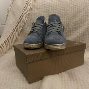 Blå sneakers från Christian Louboutin - Säljer ett par blå sneakers från Christian Louboutin med klassisk röd sula. Skorna har snörning och är tillverkade i mocka med rund tå och platt sula. Kommer med originalkartong och dustbag. Perfekt för dig som gillar exklusiva märken och vill sticka ut. Pris kan diskuteras.det svarta på skon är hål för jag eldade på dom men inga större problem än det!hör av er vid köp eller frågor!