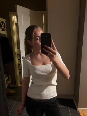 Vit ribbad topp med fyrkantig hals - Säljer en vit ribbad topp med korta ärmar och snygg fyrkantig halsringning. Toppen har en slim passform och är tillverkad i mjuk bomull som sitter skönt mot kroppen. 🤩