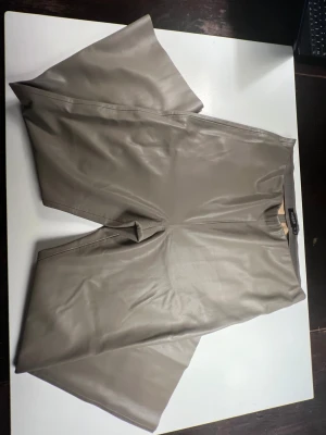 Beige SOAKED byxor i skinnimitation XXL - Snygga beige byxor från Soaked in Luxury i storlek XXL. Byxorna har ett wide fit och är gjorda i mjuk skinnimitation med elastisk midja. Perfekta för dig som gillar trendiga och bekväma plagg med lite extra edge.