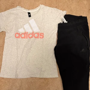 Ljusgrå Adidas t-shirt med logga - Snygg ljusgrå t-shirt från Adidas med stor vit och rosa logga på bröstet. Klassisk rund hals och korta ärmar. Perfekt för dig som gillar sportig stil och vill ha något bekvämt och enkelt. Materialet är mjuk bomull som känns skönt mot huden.