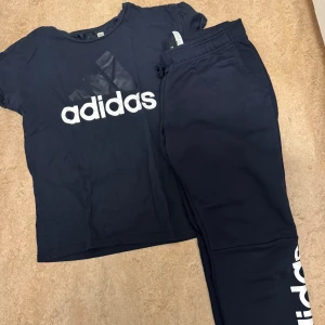 Mörkblå Adidas t-shirt med logga - Snygg mörkblå t-shirt från Adidas med stor vit logga framtill. Klassisk rund hals och korta ärmar, perfekt för träning eller chill. Mjuk bomullskvalitet som känns skön mot huden. Enkel och sportig stil som funkar till det mesta.