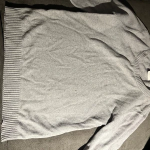 Grå stickad tröja från VILA - En enkel och stilren grå stickad tröja från VILA i storlek S. Tröjan har rund hals, långa ärmar och breda ribbade muddar vid nederkant och halsringning. Perfekt för dig som gillar en clean look och vill ha något mjukt och bekvämt.