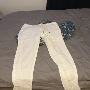 Vita linnebyxor med snörning - Snygga vita linnebyxor från Equipe med avslappnad passform och snörning i midjan. Byxorna har både knapp och dragkedja framtill samt bakfickor med träknappar. Perfekta för varma dagar och chill stil. Små i storleken