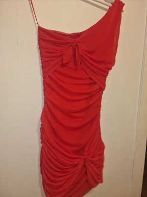 Röd one shoulder klänning - Snygg röd kortklänning med one shoulder-design. Den har draperad effekt & knytningar framtill. Perfekt för höstens fester och event.