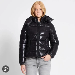 BYTE!! - Säljer en svart, glansig pufferjacka med huva och dragkedja framtill. Jackan har en quiltad design och två sidofickor med dragkedja. Perfekt för kalla dagar och har en snygg, modern look som passar till jeans eller andra outfits.