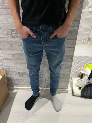 Dsquared2 blå jeans - Snygga Dsquared2 Busted jeans i klassisk blå tvätt med diskreta slitningar och smal passform. Jeansen har fem fickor, knappgylf och brunt läderpatch bak i midjan. Tillverkade i slitstarkt bomullsmaterial och har en modern, slim siluett.