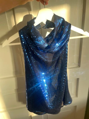 Blå glittrig halterneck topp - Säljer en blå glittrig halterneck topp med paljetter och kedjedetaljer på sidorna. Toppen har en öppen rygg med en snygg draperad halsringning💙Lappen är avklippt men den är från Zara i storlek S