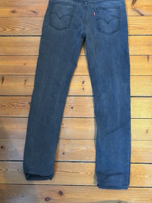 Levi's 512 mörk svarta jeans - Säljer ett par Levi's 512 jeans i svart tvätt med klassisk femficksdesign och raka ben. Jeansen har en slim passform och är tillverkade i mjukt bomullsmaterial med lite stretch för extra komfort. Perfekt för dig som gillar en stilren och enkel look.