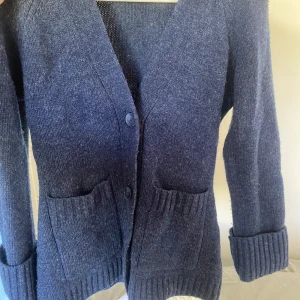 Marinblå stickad kofta från Wera - Säljer en marinblå stickad kofta från Wera i storlek XS. Koftan har två stora fickor framtill, ribbade muddar och stängs med två knappar. Perfekt för dig som gillar en chill och klassisk look med lite extra mysfaktor. Har lite noppror men inget man tänker på