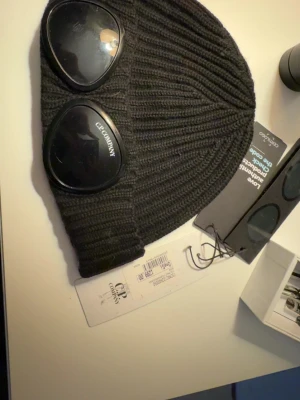 Svart stickad mössa från C.P. Company - Svart ribbstickad mössa från C.P. Company köpt för 1299 finns repor på ena glaset men syns knappast kan fraktas och mötas i Stockholm 