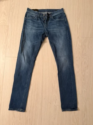 Blå jeans från Dondup (Nya) - Snygga blå jeans från Dondup, modell George . Jeansen har klassisk femficksdesign, orangea sömmar på bakfickorna och knappgylf. Passformen är tight och materialet är mjukt denim i bomull. Perfekt för dig som gillar smal siluett och italiensk design.