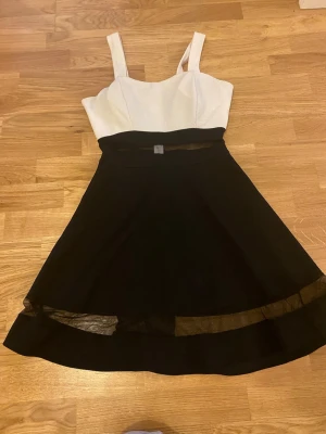Svart och vit kortklänning med meshdetalj och inbyggd bh - Snygg kortklänning med vit överdel och svart kjol. Klänningen har breda axelband och en markerad midja med transparent meshdetalj både vid midjan och längst ner på kjolen. Klänningen har en inbyggd bh🤩 Perfekt till nyår!! OBS se sista bilden finns ett hål i klänningen därmed säljer jag den billig!