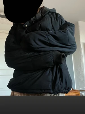 Svart pufferjacka med huva - Säljer en svart pufferjacka med huva. Jackan har en oversized passform och är perfekt för kalla dagar. Den är quiltad och har dragkedja framtill. Enkel och stilren design som funkar till många olika outfits.