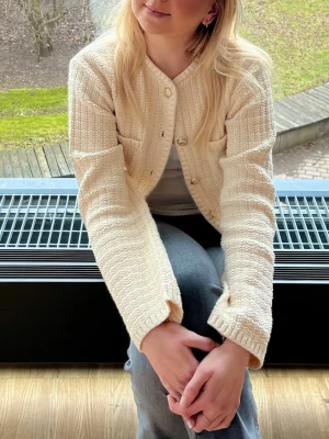 Beige/vit kofta från H&M med guldknappar - Superfin beige/vit kofta från H&M med snygga guldiga knappar och två små fickor fram. Koftan är stickad i ett mjukt material och har en croppad vibe🦢