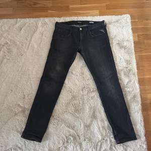 Replay Anbass svarta jeans, 32/32 - Svarta Replay Anbass jeans med snygg tvätt och klassisk femficksdesign. Slimmad passform och diskret Replay-logga på myntfickan. Jeansen är gjorda i stretchigt denim för extra komfort och har dragkedja i gylfen. Perfekta för en cool och avslappnad stil.