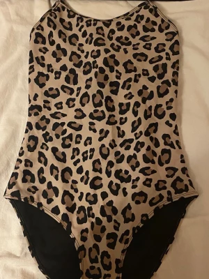 Leopardmönstrad baddräkt för barn💕 - Säljer en baddräkt för barn i storleken 146/152 med leopardmönster i beige och svart. Modellen har smala axelband som korsas i ryggen. 💕