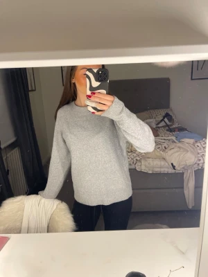 Ljusgrå stickad tröja - Mysig ljusgrå stickad tröja med rund halsringning och långa ärmar. Tröjan har en enkel och stilren design med ribbade muddar vid ärmslut och nederkant. Använd endast 1 gång