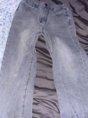 Grå jeans bage  - Säljer ett par grå jeans med klassisk femficksdesign och raka ben. Jeansen har en ljusgrå tvätt med subtila slitningar och är tillverkade i ett mjukt bomullsmaterial. Passar dig som gillar en enkel och clean look.